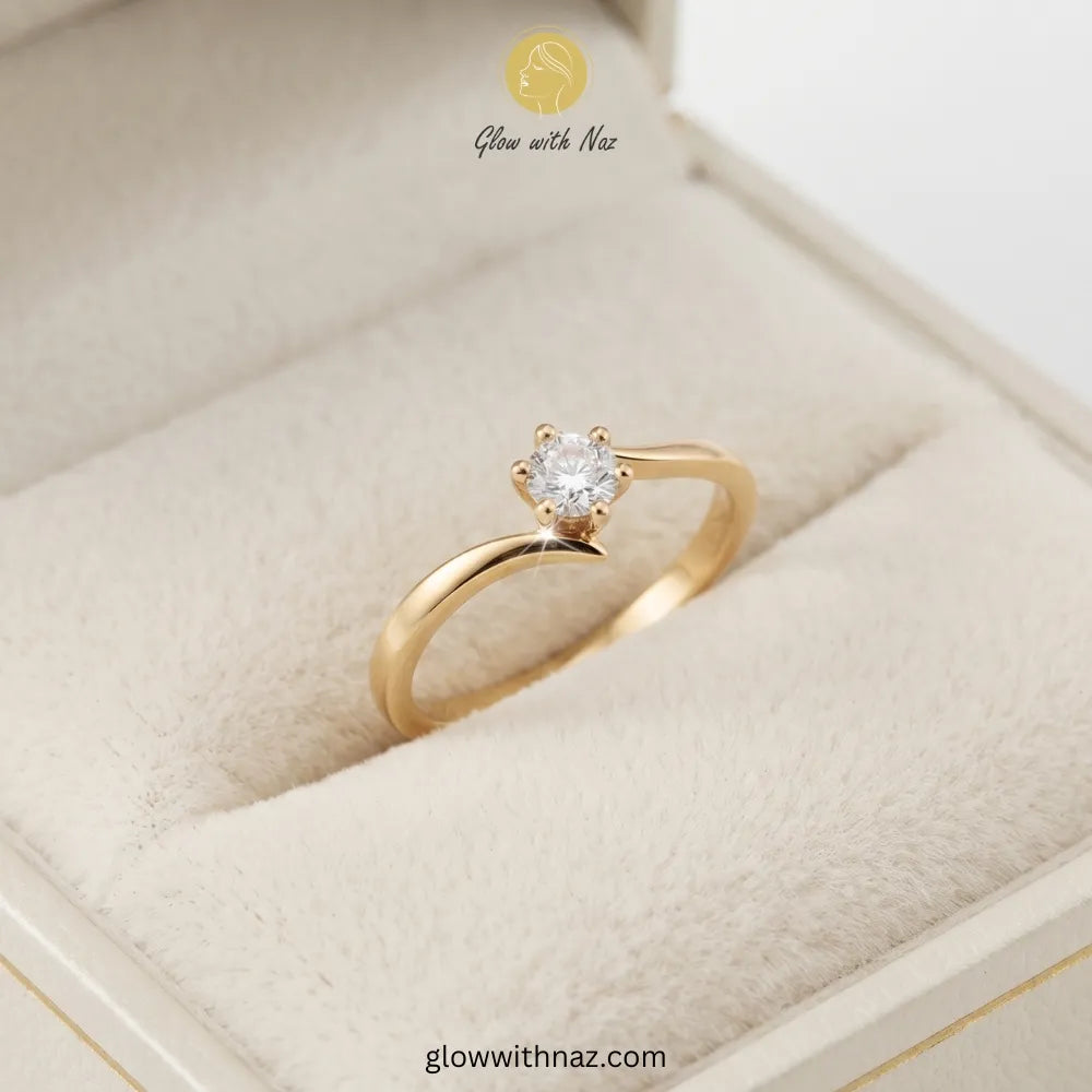 A gold solitaire engagement ring with a round-cut clear gemstone, displayed in a cream-colored velvet ring box. The brand logo 'Glow with Naz' is visible at the top and the website 'glowwithnaz.