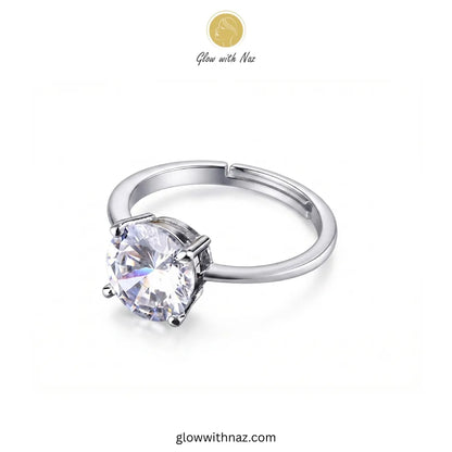 A silver-tone ring with a large round clear gemstone in a prong setting, shown on a plain white background. A small 'Glow with Naz' logo appears near the top, and 'glowwithnaz.