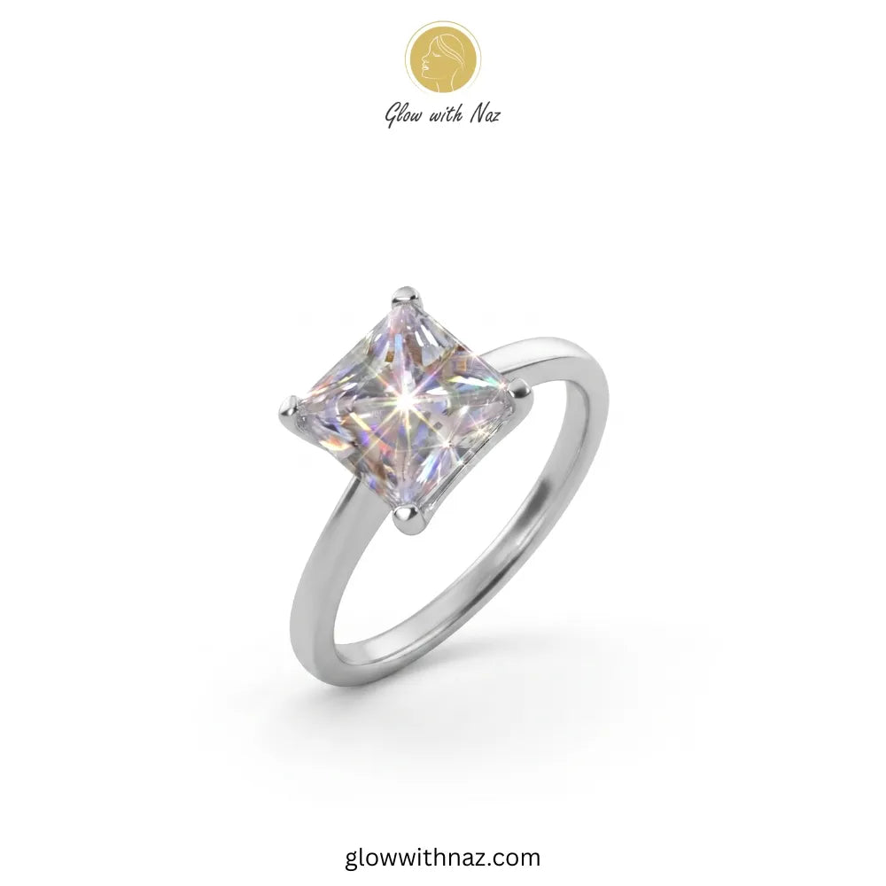 A silver-toned ring with a square iridescent gemstone, shown on a plain white background with a small 'Glow with Naz' logo at the top and the website at the bottom.