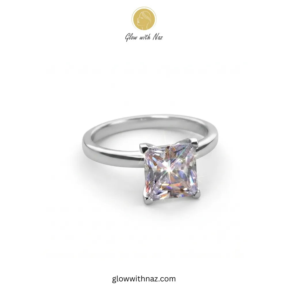 A silver band ring featuring a princess-cut clear gemstone in a four-prong setting, shown on a plain white background with a 'Glow with Naz' logo at the top.