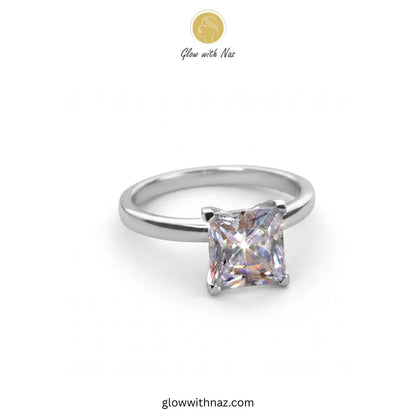 A silver band ring featuring a princess-cut clear gemstone in a four-prong setting, shown on a plain white background with a 'Glow with Naz' logo at the top.