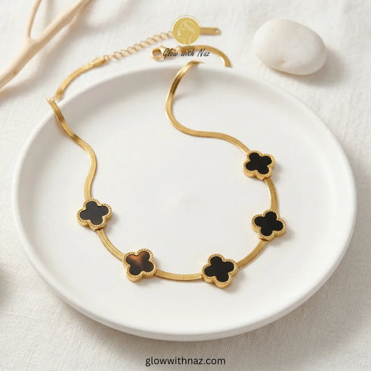 Snake Chain with Five-Motif Black Clovers Necklace Pink tulip Necklace with pink stones on a white plate, brand 'Glow with Naz' visible