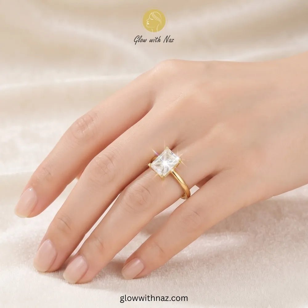 Adjustable Golden Radiant Rectangle Diamond Ring - Adjustable Golden Radiant Rectangle Diamond RingJewelryGlow With NazGlow With NazR021A gold ring with a square clear gemstone set on a person's ring finger, shown against a soft beige fabric background. The brand name 'Glow with Naz' is visible at the top. ring, girls rings, rings for girls, rings simple, simple rings, stainless steel jewelry, jewellery set, aesthetic jewelry, simple jewellery, chain, jewelry, artificial jewellery