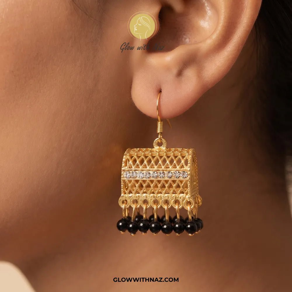 Cylinder Black Jhumka Trending Diamond & Black Drop Earrings - #Cylinder Black Jhumka Trending Diamond & Black Drop EarringsJewelryGlow With NazGlow With NazE078A close-up of a person's ear wearing a gold-toned jhumka earring with a horizontal row of clear stones and dangling black beads, against a warm skin-toned background.#