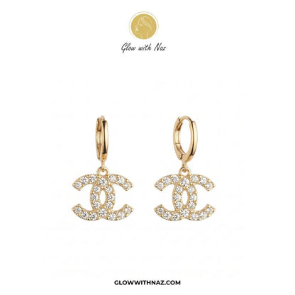 Dainty Gold Pave Channel Drop Hoop Earring - #Dainty Gold Pave Channel Drop Hoop EarringJewelryGlow With NazGlow With NazE088A pair of gold hoop earrings with interlocking CC charms paved with clear crystals, displayed on a white background with the brand logo 'Glow with Naz' at the top and 'GLOWWITHNAZ.COM' at the bottom.#