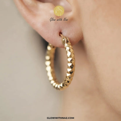 Gold Textured Diamond-Cut Bali Hoop Earrings - #Gold Textured Diamond-Cut Bali Hoop EarringsJewelryGlow With NazGlow With NazE089A close-up of a textured gold hoop earring worn on a person's ear, with a Glow with Naz logo overlay near the top of the ear and the website GLOWWITHNAZ.COM at the bottom.#