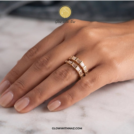 Golden Arrow Crystal Ring for Women - Golden Arrow Crystal Ring for WomenJewelryGlow With NazGlow With NazR0027A close-up of a hand wearing two stacked gold rings with rectangular clear stones, resting on a light marble surface. A logo for Glow With Naz is visible at the top, and the website glowwithnaz. ring, girls rings, rings for girls, rings simple, simple rings, stainless steel jewelry, jewellery set, aesthetic jewelry, simple jewellery, chain, jewelry, artificial jewellery