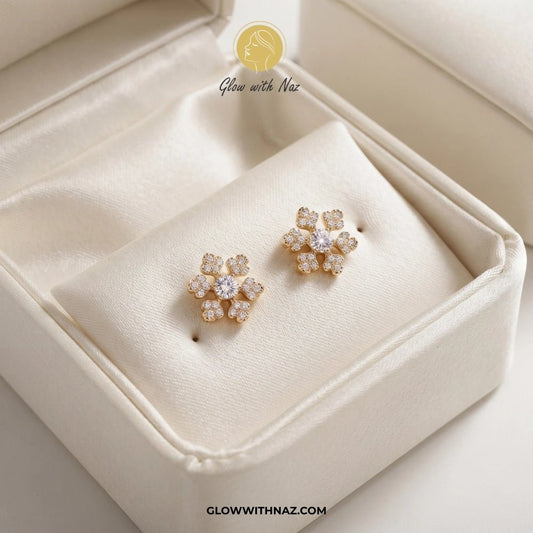 Minimal Zircon Snow Flakes Stud Earrings for Women - Minimal Zircon Snow Flakes Stud Earrings for WomenJewelryGlow With NazGlow With NazE032A pair of gold flower-shaped stud earrings with clear stones, displayed on a cream satin-lined jewelry box. A watermark logo for 'Glow with Naz' is visible at the top, and the URL 'CLOWWITHNAZ. studs earrings, small earrings, girls earrings, simple earrings, earrings for girls, black earrings, earrings, ear rings, earrings tops, stud earrings, tops earrings,
