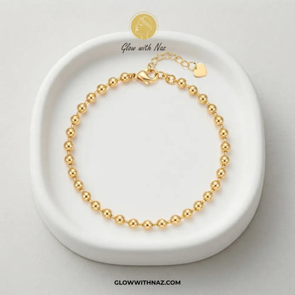 Gold ball chain bracelet displayed in a white ceramic trinket dish by Glow With Naz
