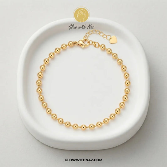 Gold ball chain bracelet displayed in a white ceramic trinket dish by Glow With Naz