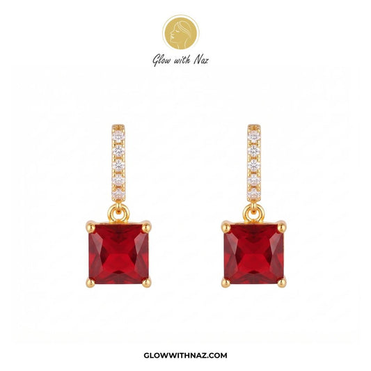 Premium Square Drop Zircon Stud Earring for Girls - Premium Square Drop Zircon Stud Earring for GirlsJewelryGlow With NazGlow With NazE035A pair of gold drop earrings featuring square-cut red gemstones, with a vertical bar of small clear stones above each red stone. The brand logo 'Glow with Naz' is visible at the top and the website 'GLOWWITHNAZ. studs earrings, small earrings, girls earrings, simple earrings, earrings for girls, black earrings, earrings, ear rings, earrings tops, stud earrings