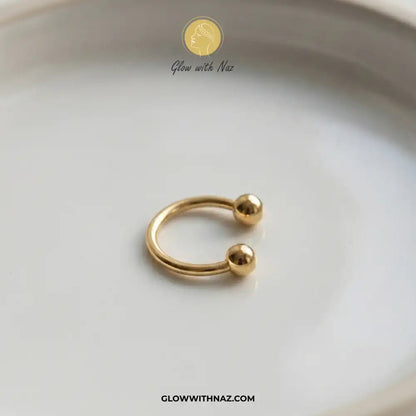 Stainless Steel Horseshoe 8.5 mm C Nose Ring & Helix Ear Piercing Jewelry - Stainless Steel Horseshoe 8.5 mm C Nose Ring & Helix Ear Piercing JewelryJewelryGlow With NazGlow With NazNR004A small gold open hoop ring with two polished ball ends, photographed on a white ceramic dish. The brand name Glow with Naz is visible as a watermark at the top, and the website GLOWWITHNAZ. nose ring, helix piercing jewelry, cartilage earring, horseshoe piercing, septum ring, stainless steel jewelry, body jewel