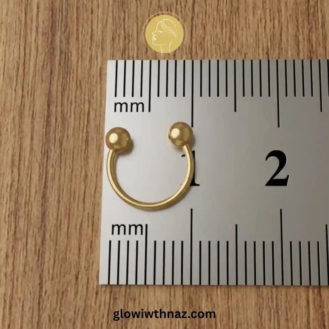 Stainless Steel Horseshoe 8.5 mm C Nose Ring & Helix Ear Piercing Jewelry - Stainless Steel Horseshoe 8.5 mm C Nose Ring & Helix Ear Piercing JewelryJewelryGlow With NazGlow With NazNR004A small gold C-shaped nose ring with two ball-ended tips placed on a metal ruler over a wood surface, with a small circular logo above and the text glowiwnnaz.com at the bottom. nose ring, helix piercing jewelry, cartilage earring, horseshoe piercing, septum ring, stainless steel jewelry, body jewelry, hypoaller