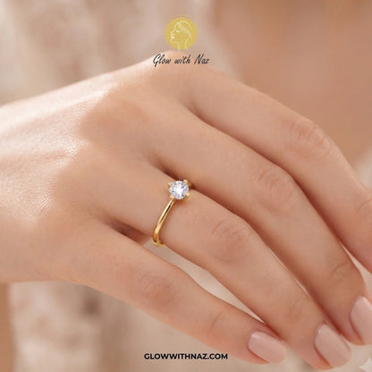 Timeless 4 Grip Diamond Ring for Women - Timeless 4 Grip Diamond Ring for WomenJewelryGlow With NazGlow With NazA gold solitaire ring with a clear round gemstone worn on a woman's finger. The image features a warm, soft-focus background and a brand watermark 'Glow with Naz' at the top and 'GLOWWITHNAZ. ring, girls rings, rings for girls, rings simple, simple rings, stainless steel jewelry, jewellery set, aesthetic jewelry, simple jewellery, chain, jewelry, artificial jewellery