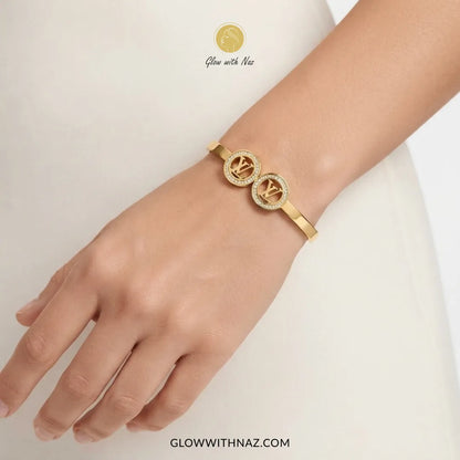 Gold twin LV medallion crystal handcuff bangle worn on wrist model by Glow With Naz