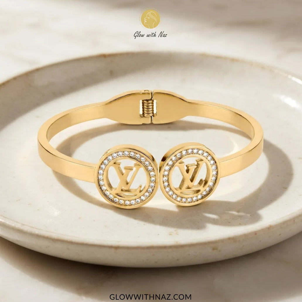 Gold twin LV medallion handcuff bangle displayed on ceramic dish by Glow With Naz
